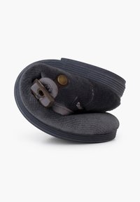 Zapatilla de lana gris con un upper suave y texturizado, que presenta una suela de goma oscura y una tira decorativa con un detalle de broche metálico.