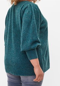 Sweter w kolorze morskim o miękkiej, teksturowanej powierzchni, z bufiastymi rękawami i zaokrąglonym dekoltem. Dół swetra jest nieco dłuższy z tyłu.