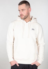 Sudadera de color beige claro, fabricada en material suave, con un bolsillo tipo canguro, cordones y un pequeño logo en el pecho. Ajuste clásico con puños de canalé.