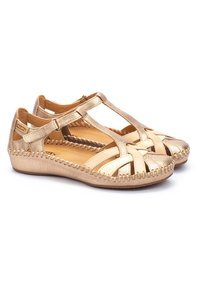 Gouden leren sandalen hebben een open teenontwerp met kruislingse banden en een gestikte accent langs de zool. Gespafsluiting bij de enkel.