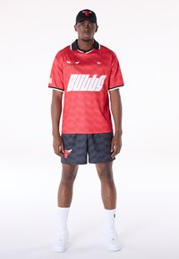 Raudonas "Chicago Bulls" džersis su juodu apykakle ir baltomis raidėmis, derinamas su tamsiomis šortais su buliuko logotipu ir tekstiniu raštu. Baltos sportbačiai.