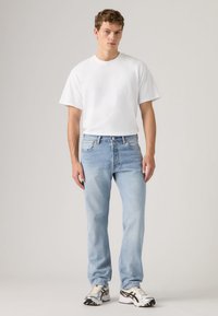 Hele sinised teksapüksid sirgjoonelise lõikega, mida on kombineeritud ühevärvilise valge ümara kaelusega T-särgiga ja mustriliste tossudega.