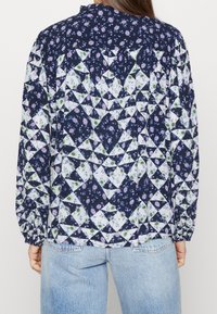 Navy blouse met lange mouwen met multi-gevlekte bloem- en geometrische ontwerpen. Heeft elastische manchetten en een licht gathered halslijn.