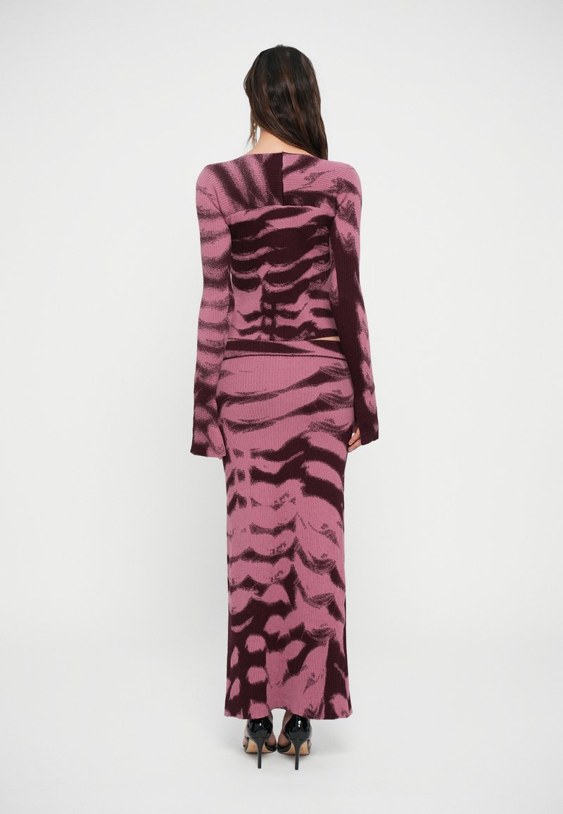 Stickad klänning med ett rosa och vinrött abstrakt mönster, åtsittande silhuett, långa ärmar och maxilängd. Texturerat tyg med ribbad yta.