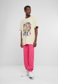 T-shirt graphique beige mettant en avant des personnages de Looney Tunes, associé à un pantalon de survêtement rose et des baskets blanches. Design décontracté et coupe relax.