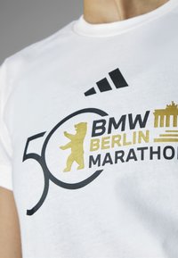 Valkoinen puuvillainen t-paita, jossa musta ja kulta printti; sisältää tekstit "BMW BERLIN MARATHON", "50" logon ja karhun siluetin.