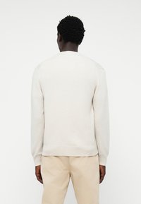 Lys grå strikkegenser med ribbestrikket kant og mansjetter. Har en klassisk rund hals og litt teksturert stoff, sammen med beige bukser.