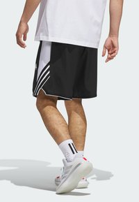 Black athletic shorts with white side stripes, paired with white socks featuring black stripes and gray athletic shoes. Background is plain.