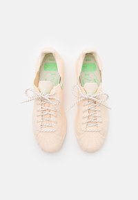 Baskets pêche clair avec une tige en tissu texturé, lacets gris et semelles intérieures vertes. Bout arrondi, silhouette basse et marquage minimal.