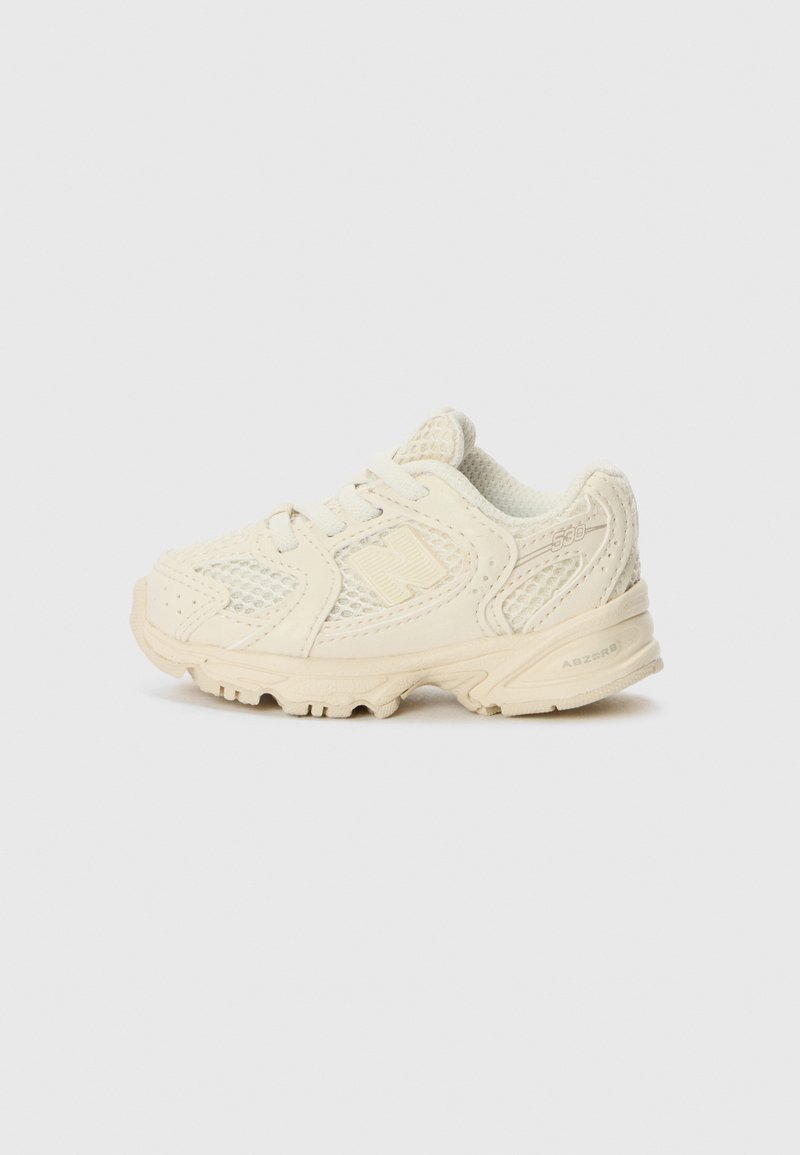 Cream-colored toddler sneakers with mesh and synthetic materials, featuring a lace-up closure and a textured rubber sole.