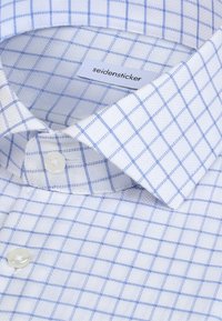 Chemise blanche à motif à carreaux bleu, col boutonné et étiquette de marque "seidensticker" à l'intérieur du col.