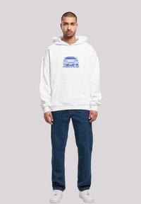 White cotton hoodie with a front kangaroo pocket, featuring a blue graphic design of a retro car and the text "Retro Car." Pair of blue jeans.