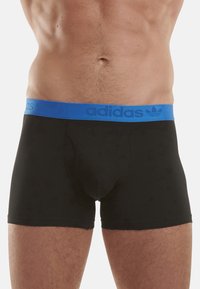 Boxer-culottes noires avec une ceinture élastique bleue portant le texte et le logo "adidas". Tissu lisse avec une coupe ajustée.