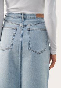 Jupe en denim bleu clair avec taille haute, deux poches arrière et coupe droite. Coutures contrastées notables et détail en cuir.