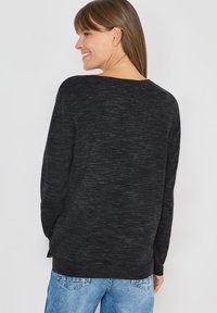 Zwarte gebreide trui met een gestructureerde stof, ronde halslijn, lange mouwen en een losse pasvorm. Gecombineerd met lichtblauwe denim jeans.