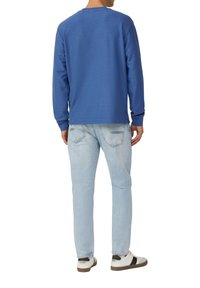 Niebieska, teksturowana, długoramienna bluza z okrągłym dekoltem, zestawiona z jasnoniebieskimi dżinsami i białymi trampkami z ciemnymi akcentami i sznurowadłami.