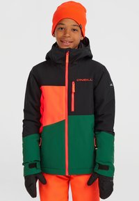 Färgglad skidjacka med svarta, orange och gröna paneler, med dragkedja framtill, huva och elastiska ärmar. Svarta handskar fulländar outfiten.