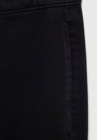 Gros plan sur un pantalon en denim noir montrant la poche et les coutures détaillées sur un tissu texturé.