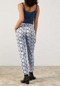 Marineblauwe tanktop gecombineerd met aansluitende witte en marineblauwe slangenpatroon broek. Zwarte enkellaarsjes met een forse hak maken de look af.