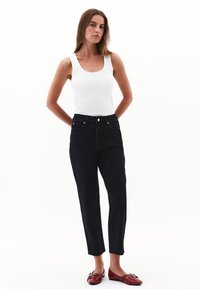 Svarta denim jeans med hög midja och rak ben, kombinerat med en tät vit tanktop. Modellen bär röda ballerina-skor med dekorativa detaljer.