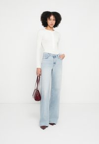 Biely top s dlhými rukávmi a zapínaním vpredu, doplnený svetlomodrými džínsami s širokými nohavicami. Celok dotvára malá bordová kabelka.