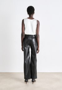 Black leather high-waisted trousers with wide legs and visible stitching details, paired with a cream sleeveless top, viewed from the back.