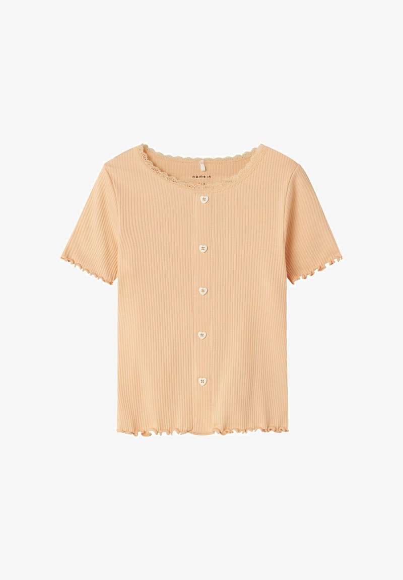 Breskve obarvana kratka majica s rebrastim uzorkom, z okroglim izrezom in nabranim robom. Ima šest gumbov v obliki srca spredaj.