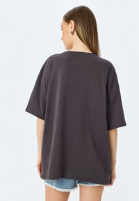 T-shirt en coton gris foncé surdimensionné avec des manches courtes, un col rond et une coupe décontractée. Assorti avec un short en denim déchiré.