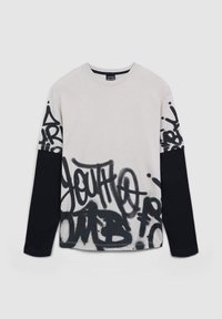 Koszulka z długim rękawem w kolorze kremowym i czarnym. Posiada czarne wzory w stylu graffiti na przodzie, z kontrastującymi jednolitymi czarnymi rękawami. Wykonana z bawełny.