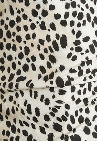 Gros plan d'un tissu blanc avec des taches noires irrégulières dans un motif léopard, montrant de légers plis et la texture.