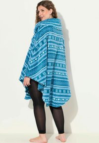 Poncho in fleece turchese con motivi geometrici e fiocchi di neve bianchi, dotato di un ampio colletto e un orlo asimmetrico fluente.