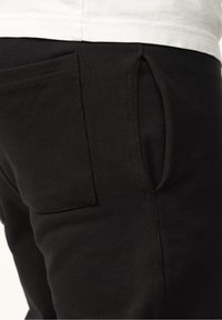 Black jogger pants with a soft texture, featuring a rear pocket and a neat seam detail. Designed with practical side openings.