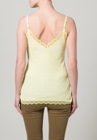 Ljusgul tanktop med spetsdetaljer längs halsringningen och fållen. Har justerbara axelband och en figursydd ribbad textur.