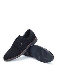 Un paio di scarpe eleganti da uomo in suede nero con lacci e suole in gomma, una scarpa in posizione verticale e l'altra che mostra il motivo della suola.