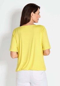 Geel T-shirt met korte mouwen, een losse pasvorm en een brede halslijn, gemaakt van een gladde stof, gedragen met witte broek.