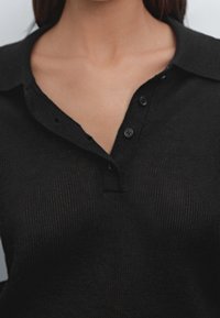 Mustat neulepikee, jossa on kaulus, kolme nappia kaula-aukossa ja teksturoitu kangas.