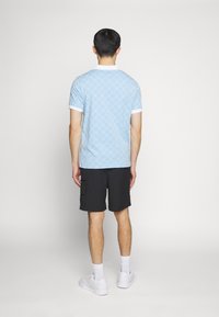 Himmelblaues Polohemd mit kurzen Ärmeln und Rautenmuster, weißer Kragen und Akzente an den Ärmeln, kombiniert mit schwarzen Cargo-Shorts und weißen Sneakers.