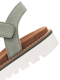 Grüner Wildleder-Knöchelriemen auf braun gepolstertem Fußbett mit weißer, gerillter Plateausohle und grünem Rand.