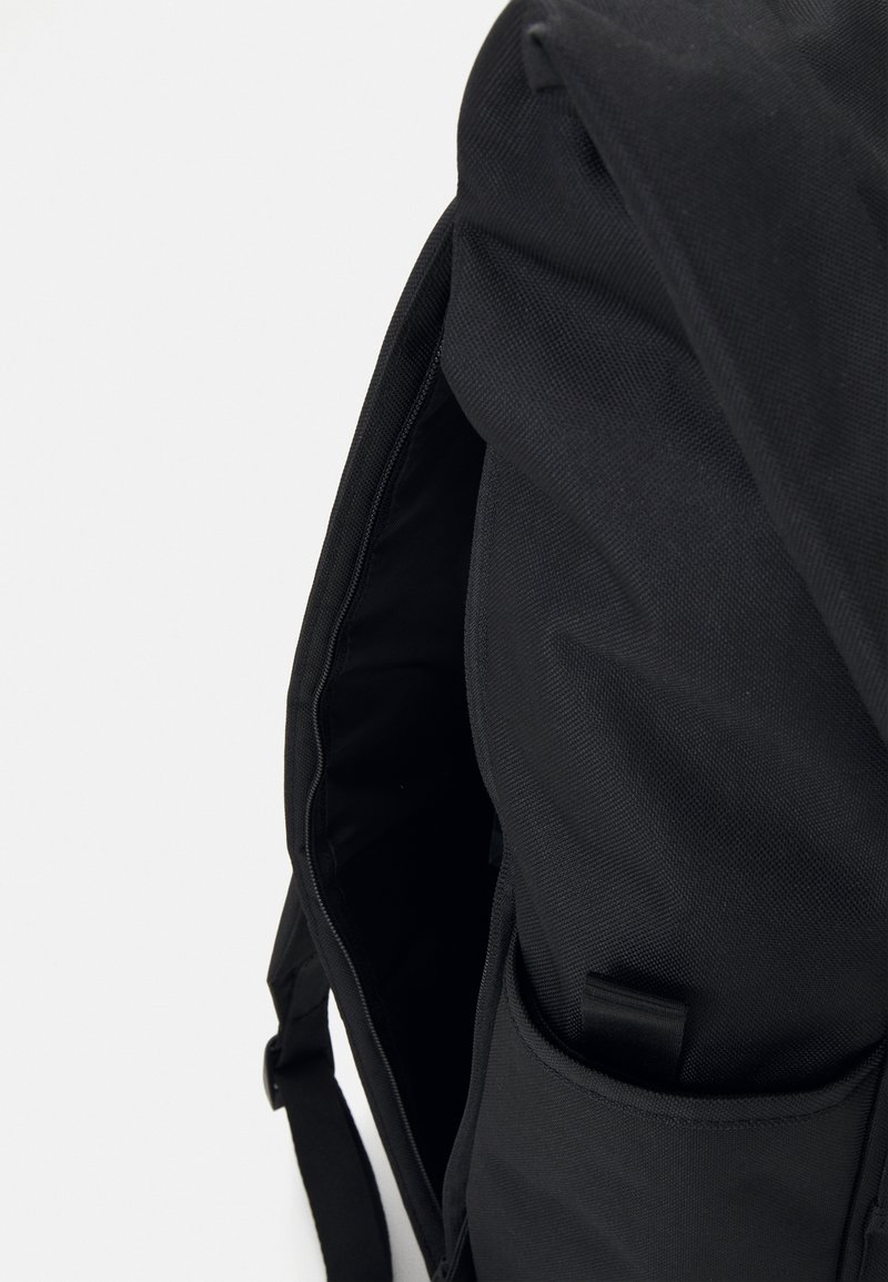 Sort rygsæk med tekstureret stof. Har en lynlåsåbning, indre lomme og justerbare stropper. Enkel, funktionel design.