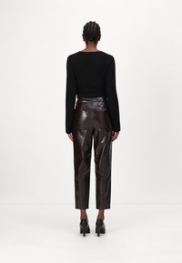 Schwarzes Langarmshirt kombiniert mit hochtaillierten, dunkelbraunen Hosen im Krokodilmuster und schwarzen High Heels, von hinten betrachtet.