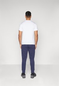 Valge lühikeste varrukatega T-särk, mille juurde on sobitatud tumesinised dressipüksid, millel on elastsed mansetid ja mis on valmistatud pehmest kangast, sobides igapäevaseks kandmiseks.