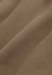 Close-up van beige gestructureerde stof met een fijn gebreid patroon en zachte plooien die diagonale schaduwen creëren.