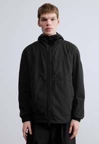 Must tuulekindel jakk kõrge kraega, esikäepidemega lukuga, elastsete varrukaservadega ja tekstuurse viimistlusega. Minimalistlik disain ilma nähtavate logodeta.