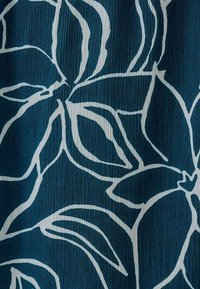 Strukturerad tyg med en blå bakgrund och djärva vita blommönster, som visar kurviga former och intrikata detaljer.