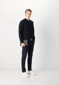Marinblå zip-neck pullover i bomullsblandning med texturerad tyg. Kombinerad med mörka byxor, vita sneakers och håller i en svart läderklutch.