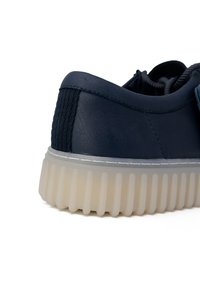 Sneaker in pelle blu navy con un pannello testurizzato sul tallone, suola in gomma traslucida con dettagli a righe e design lacciato.