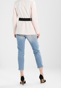 Jasnoróżowa marynarka z czarnym paskiem, dopasowana w talii, zestawiona z jasnoniebieskimi dżinsami z surowym wykończeniem u dołu oraz czarnymi butami na wysokim obcasie.