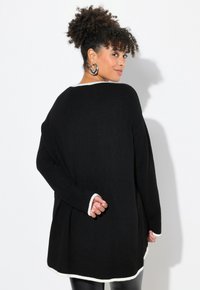 Schwarzer Pullover mit langen Ärmeln und lässigem Schnitt, mit weißen Akzenten am Rundhalsausschnitt und Saum. Weicher Stoff, minimalistisches Design und seitliche Taschen.