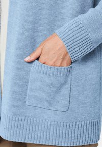 Hellblau gestrickte Cardigan mit gerippten Bündchen und Saum, ausgestattet mit einer sichtbaren Vordertasche, strukturiertem Stoff und klaren Linien.