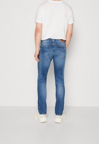 Ljusblåa denimjeans med smal passform, med två bakfickor och en brun läderetikett i midjan. Bärs med en enkel vit t-shirt.